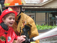 A happy child helps a fireman with his firehose